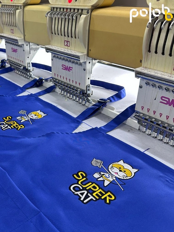 ตัวอย่างผ้ากันเปื้อนปักโลโก้ Super Cat ด้วยเครื่องปักอุตสาหกรรมในโรงงาน POLOBB